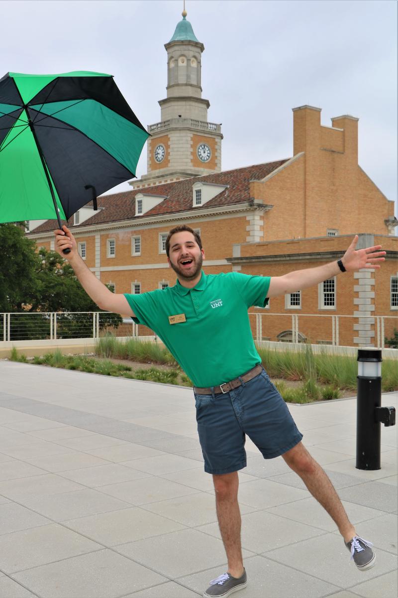A UNT Orientation Leader holding an open umbrella on the roof of the Union, with the camera pointed toward Hurley.
